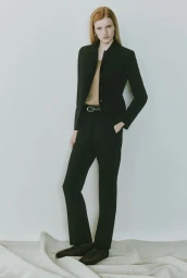 Model with red hair wearing a black suit jacket and matching trousers against a pale background for Theory lookbook