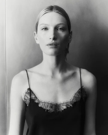 Black and white portrait of a blonde-haired woman in a lace-trimmed camisole against a blurred neutral background, medium shot.