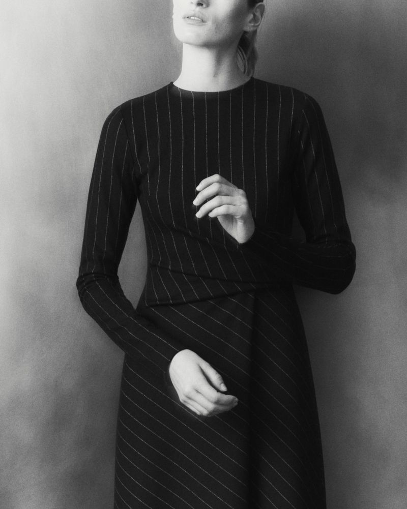 Elegant woman in a black pinstripe dress poses against a neutral background, showcasing the sophisticated fabric and design.