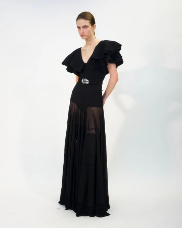 Model wearing a black ruffled evening gown with sheer lower skirt and belt against a plain white background