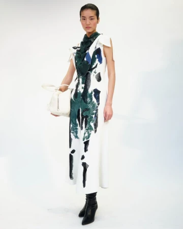 Model in printed white dress holding a white handbag against a plain background