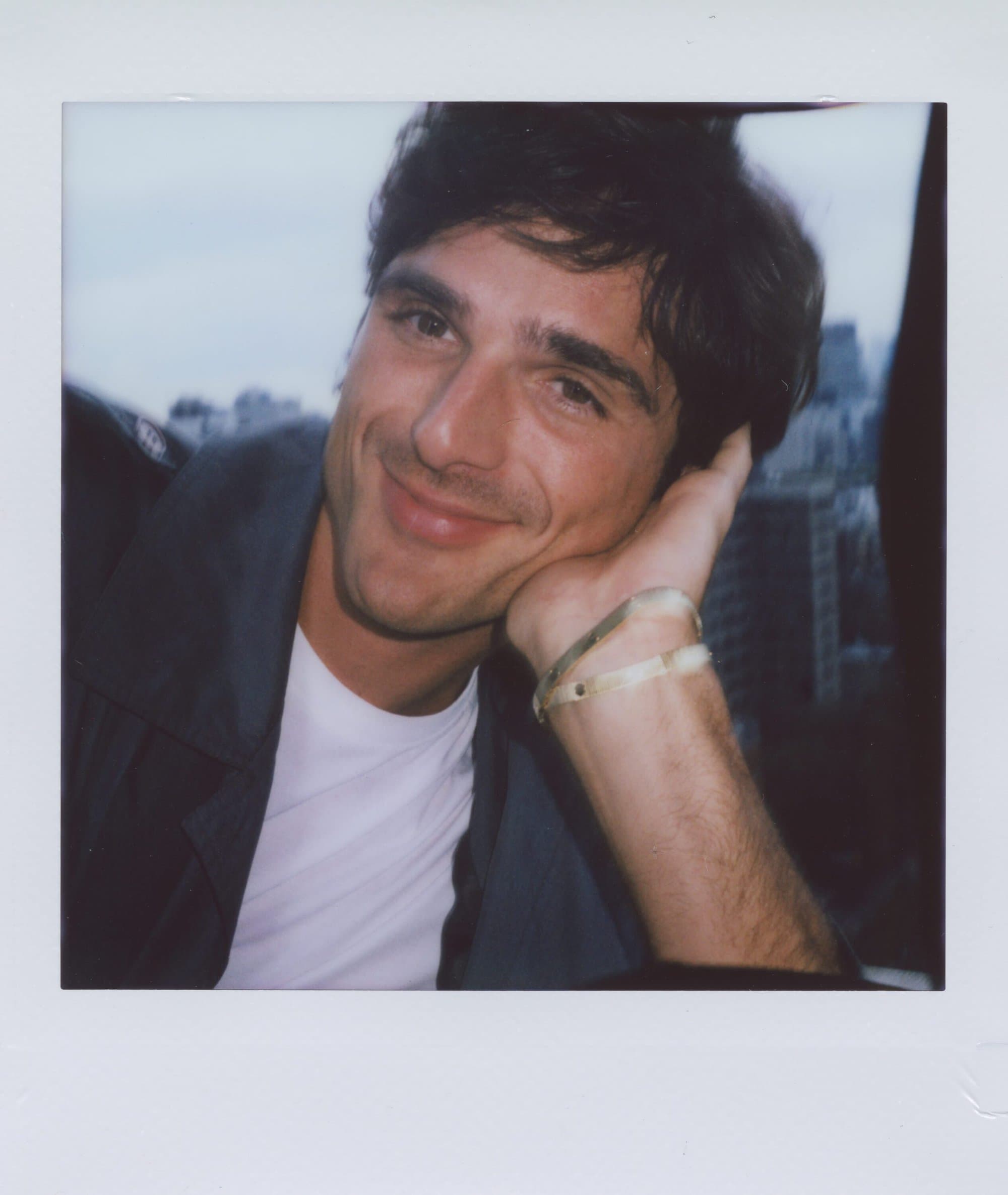 Polaroid photograph of Jacob Elordi resting his chin on his hand, wearing a white t-shirt and dark jacket.