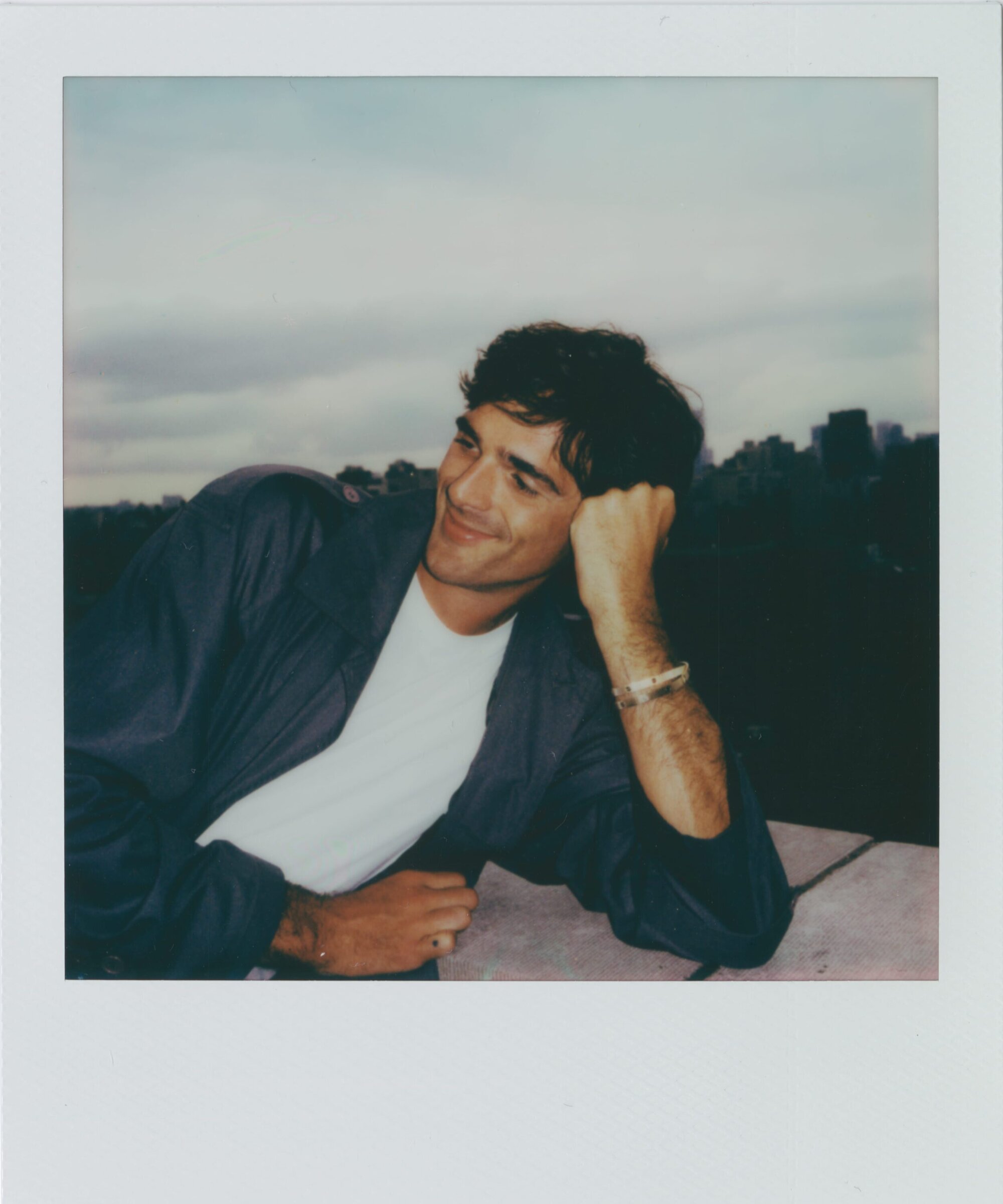 Jacob Elordi leaning on a ledge with a city skyline behind him in a polaroid photograph for Cartier Love Unlimited.