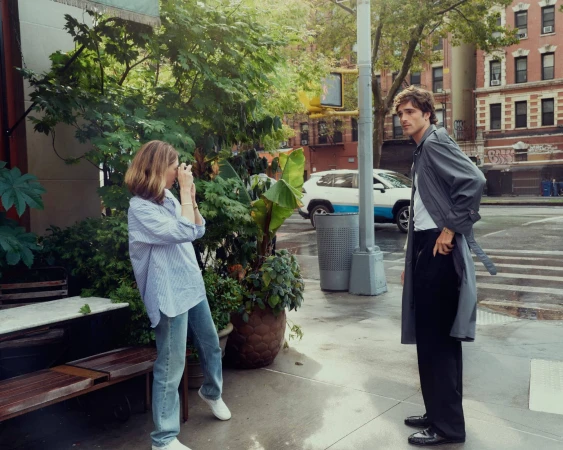 Sofia Coppola taking a photo of Jacob Elordi wearing a grey trench coat on a city street for Cartier