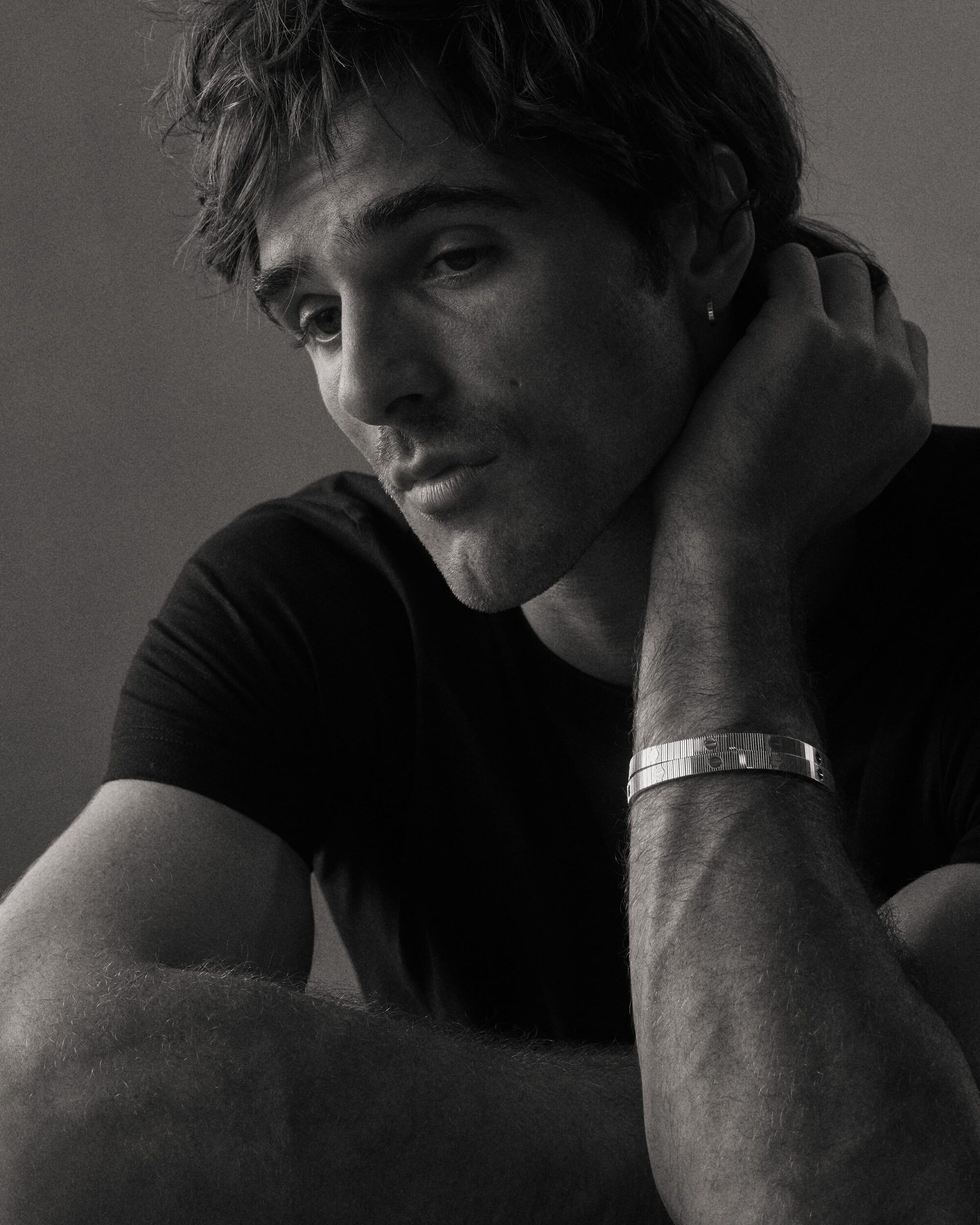 Black and white portrait of a young adult man with dark hair and a bracelet, looking off to the side in a photo studio setting.