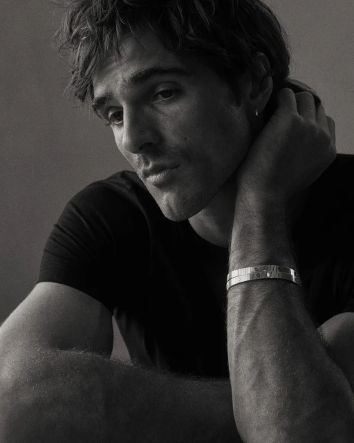 Black and white portrait of a young adult man with dark hair and a bracelet, looking off to the side in a photo studio setting.