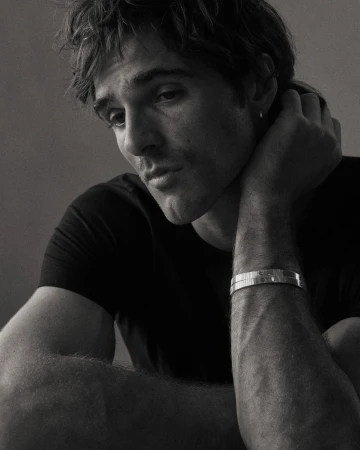 Black and white portrait of a young adult man with dark hair and a bracelet, looking off to the side in a photo studio setting.