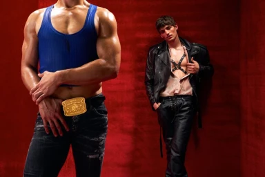 Two male models posing against a rich red backdrop for Dsquared2 featuring a blue tank top and black leather jacket