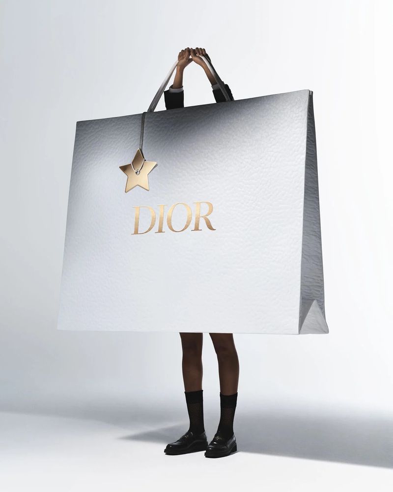 Oversized Dior shopping bag held by a person in a studio, showcasing fashion and luxury branding with a star-shaped charm accessory.