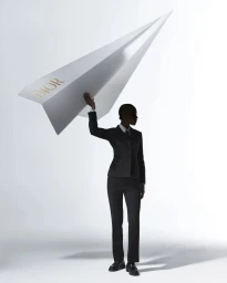 A person in a black suit holding up a large white paper airplane with gold Dior branding against a white background