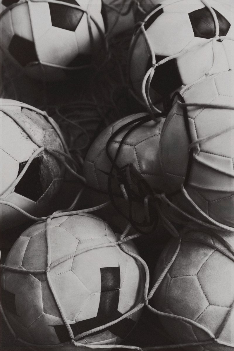 Black and white photo featuring a pile of soccer balls contained in a net, creating a textured and visually interesting composition.