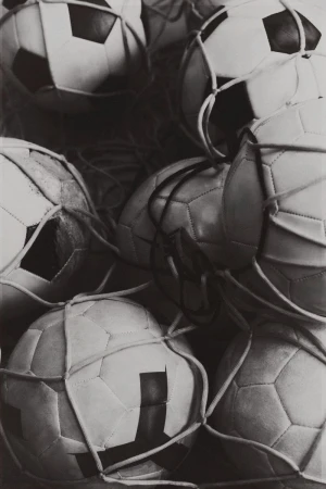 Black and white photo featuring a pile of soccer balls contained in a net, creating a textured and visually interesting composition.