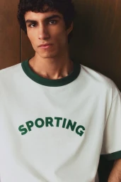 Young man with dark hair wearing a white t-shirt with green trim and the word Sporting printed across the chest