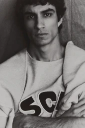 Close-up monochrome portrait of a young male model with dark curly hair posing in a crewneck sweatshirt.