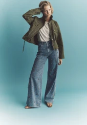 Model in olive green jacket and embellished wide-leg jeans against blue gradient backdrop