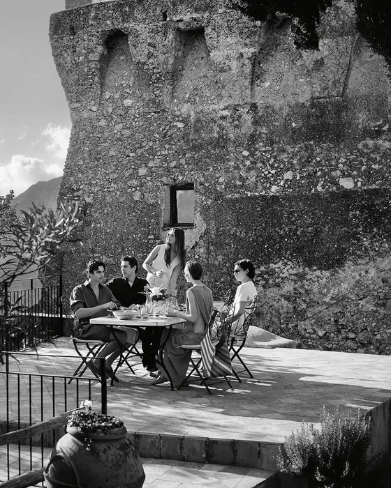Group of five models gathered around an outdoor table against a rustic stone wall for Tod's S/S 2026 campaign.