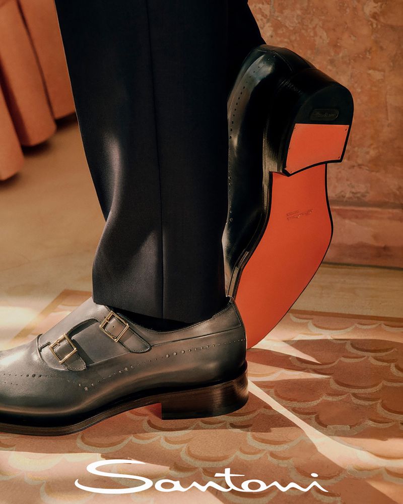 Elegant monk strap dress shoes in grey leather with gold buckles and black leather shoes with bright orange sole in fashion product shot.