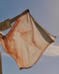 Person holding up a patterned silk scarf against a clear blue sky for Santoni Spring Summer 2026 campaign.