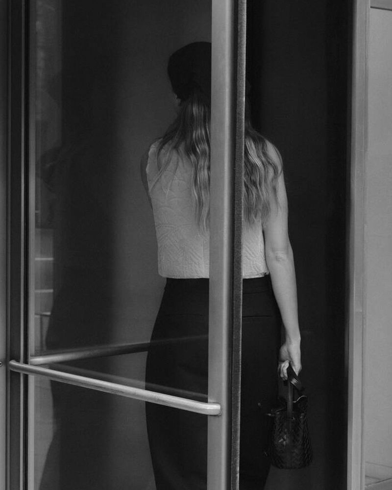 Back view of a woman in black and white, seen through an open doorway, showcasing a minimalist aesthetic.