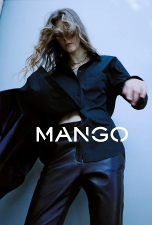Fashion shot: blonde model in unbuttoned black shirt and black pants poses in a studio with simple jewelry, hair covering her face.