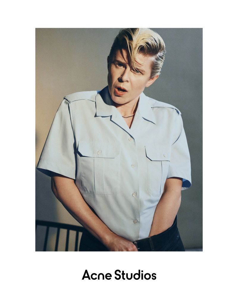 Close-up of an adult female with blonde hair, wearing a light blue short sleeve shirt, looking to the side in a studio setting.
