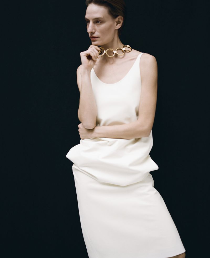 Model wearing a white dress and chunky gold link choker necklace against a black background
