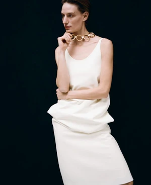 Model wearing a white dress and chunky gold link choker necklace against a black background