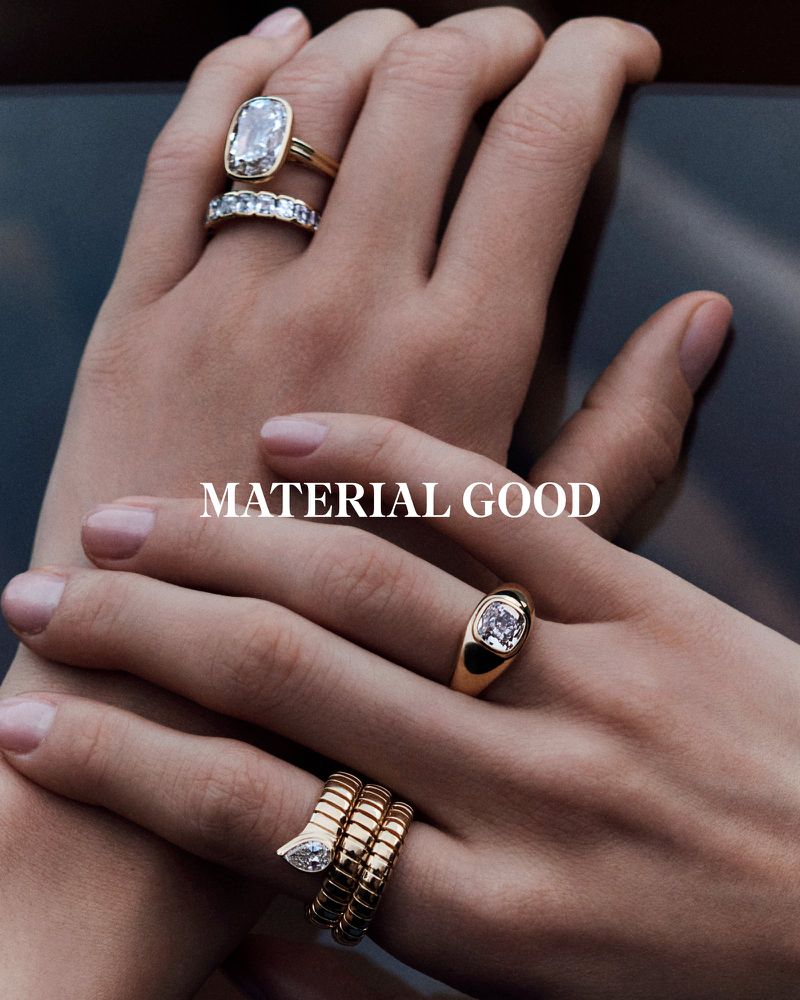 Close-up of four gold rings on woman's fingers. Rings feature diamonds. Fingers are posed against a dark surface with soft lighting.