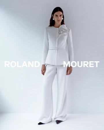 Fashion shoot featuring a woman wearing a white Roland Mouret blazer with a flower detail and wide-leg pants, posing in a studio.