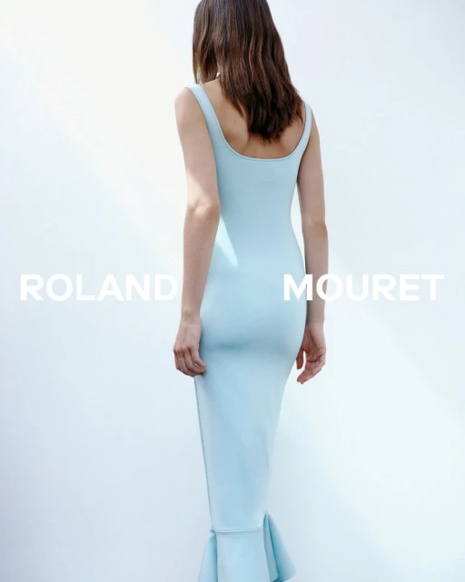 Woman in a fitted light blue dress stands against a bright white background, back to camera, minimalist fashion photography.