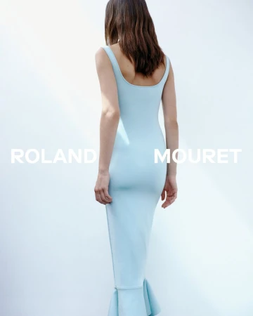 Woman in a fitted light blue dress stands against a bright white background, back to camera, minimalist fashion photography.