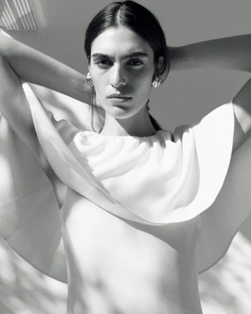 Model with hands behind head wearing white top and silver earrings in black and white