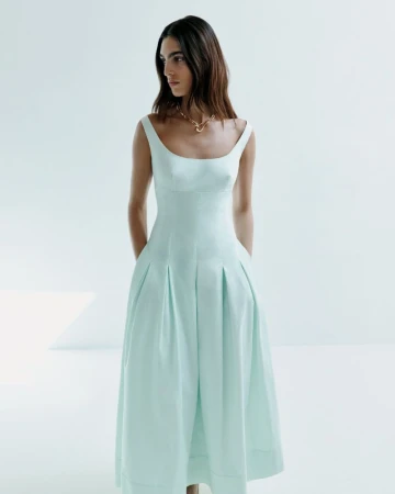 Model wearing a pale green scoop neck midi dress with pleated skirt against a bright white background