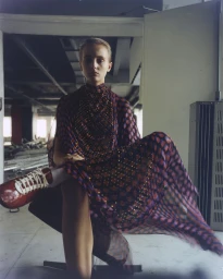 Model wearing a patterned dress and red sneakers seated in an industrial interior for D Repubblica