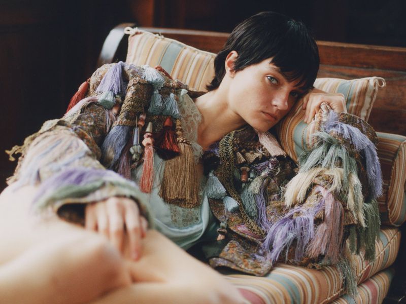 Woman lies on striped lounge chair wearing a tassel jacket in an interior setting, close-up shot with medium depth of field.