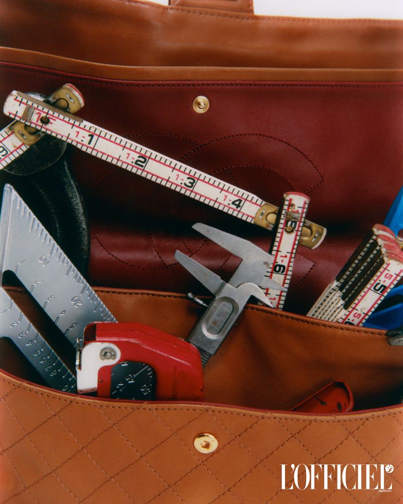 Designer handbag with measuring tools inside. A tan quilted leather purse holds a folding ruler, angle finder, and caliper.