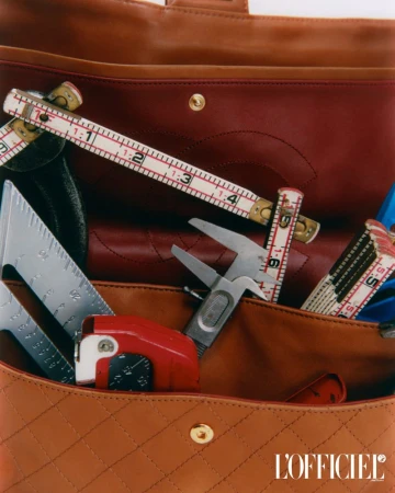 Designer handbag with measuring tools inside. A tan quilted leather purse holds a folding ruler, angle finder, and caliper.