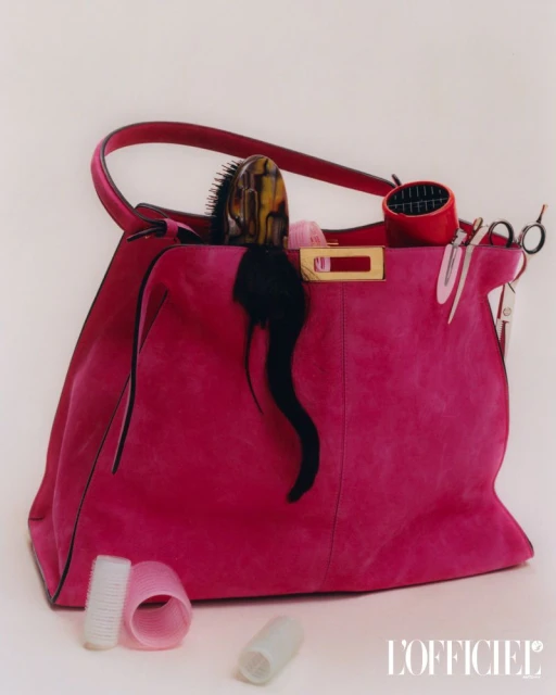 Hot pink handbag with a collection of hair styling tools overflowing from its top, including hair brushes, rollers, and scissors.