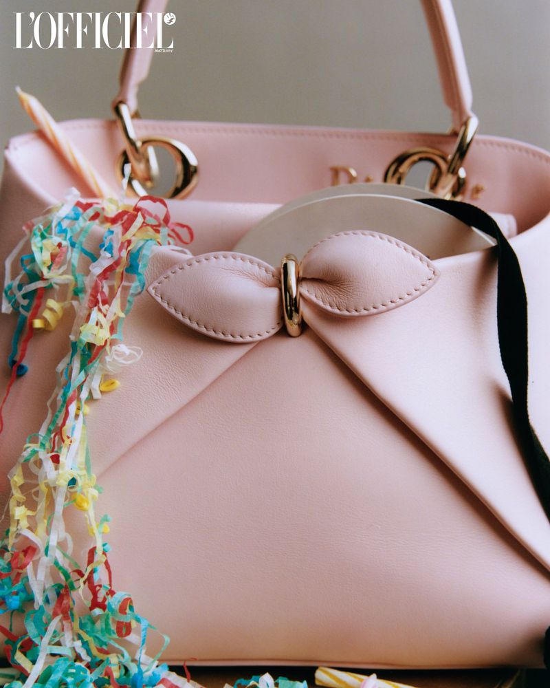 Close-up of a pink leather purse decorated with colorful confetti and a candle. The purse has gold hardware and a bow detail.