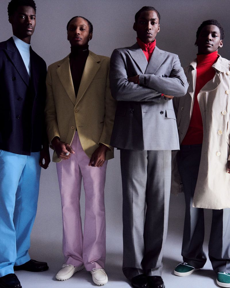 Group of four young Black men in formal suits and turtlenecks posing in front of a neutral backdrop in a studio setting.