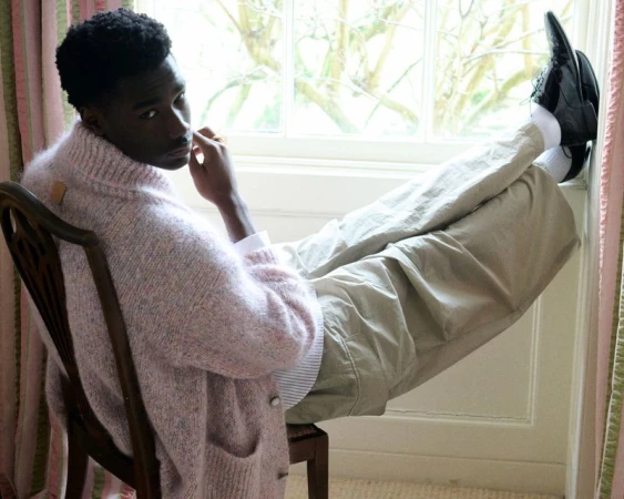 Portrait of an African American man in a pink cardigan sitting by a window in a neutral setting with natural light.