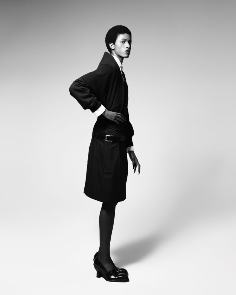 Elegant portrait of a Black fashion model in a black dress and patent-leather heels against a bright studio backdrop in black and white.