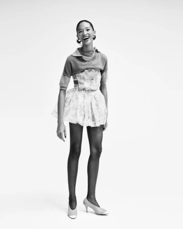 Smiling female model wearing a layered patterned outfit and pumps against a bright white background for Elle Belgium.