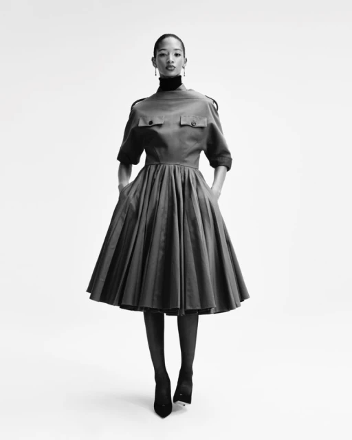 Black and white fashion shot of a Black female model in a fit-and-flare dress with short sleeves, black tights, and black high heels.