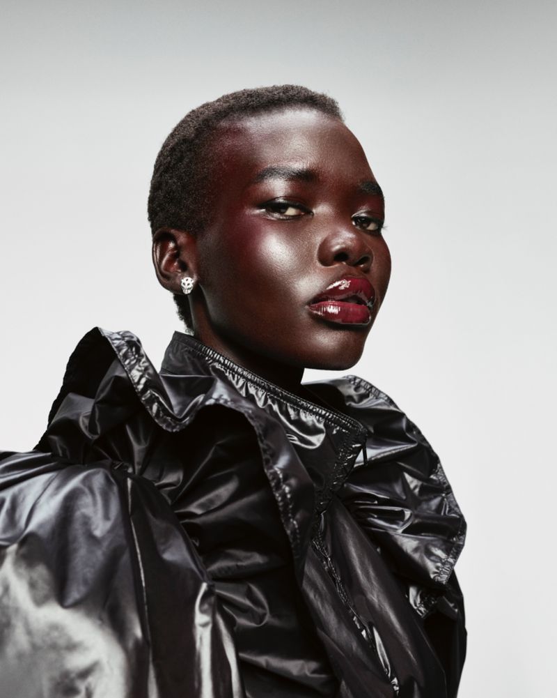 Close-up portrait of a Black woman with short hair, wearing a glossy black jacket and bright red glossy makeup in a studio setting.
