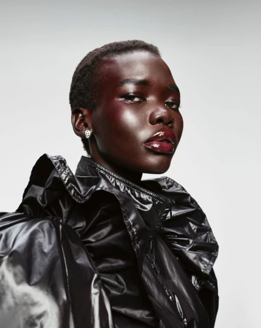Close-up portrait of a Black woman with short hair, wearing a glossy black jacket and bright red glossy makeup in a studio setting.