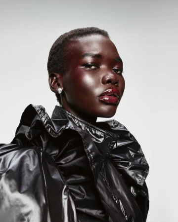 Close-up portrait of a Black woman with short hair, wearing a glossy black jacket and bright red glossy makeup in a studio setting.