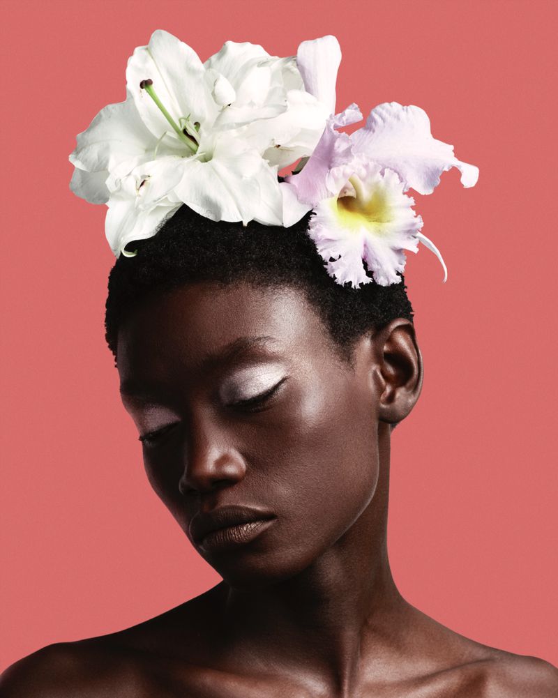 Portrait of a short-haired African-descent adult woman with closed eyes. She is adorned with white and light-purple flowers.