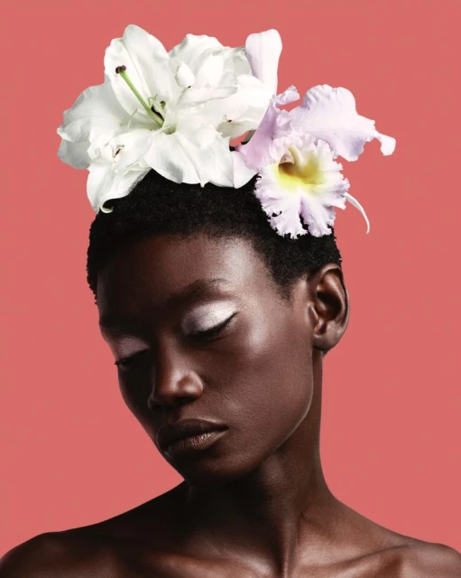 Portrait of a short-haired African-descent adult woman with closed eyes. She is adorned with white and light-purple flowers.