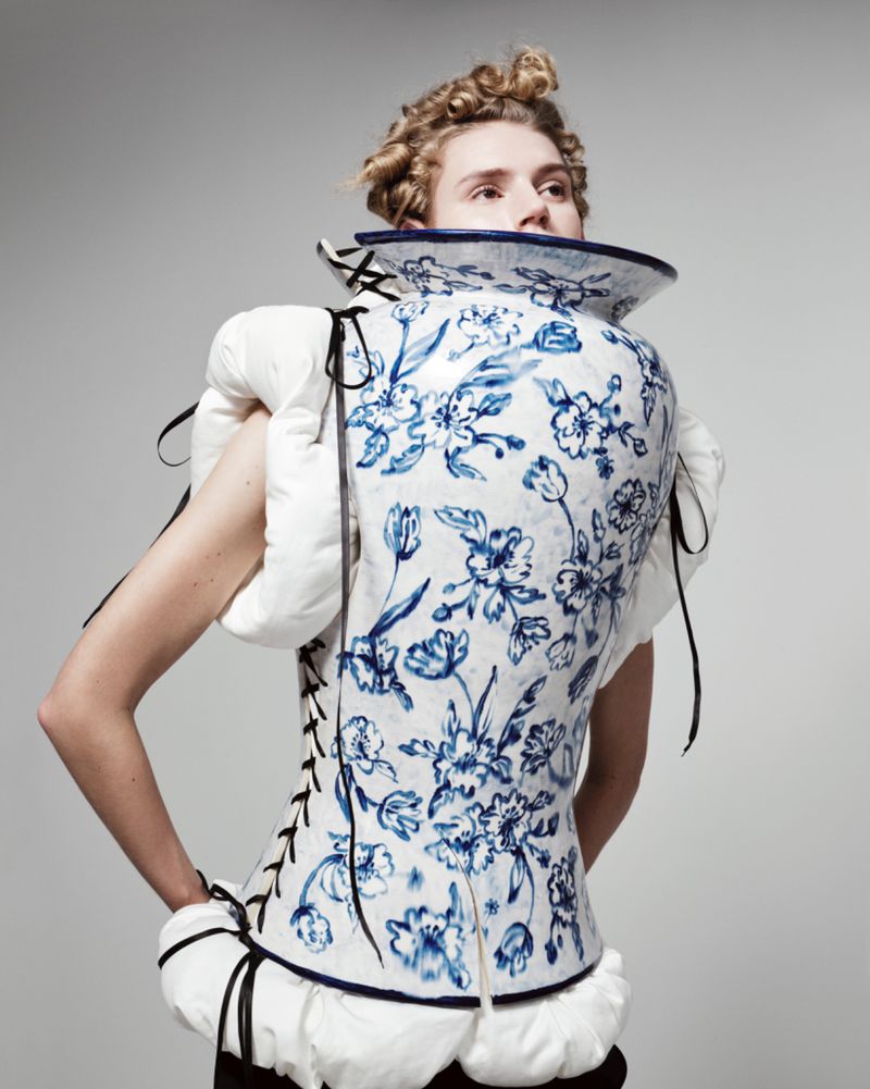Unique fashion portrait of a person wearing a vase-like floral corset with puffed sleeves against a neutral background in a studio.